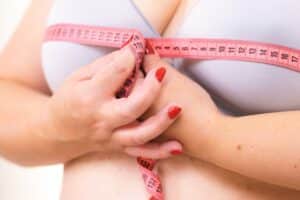 A woman considering breast reduction wrapping a tape measure around her breasts