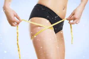 A cropped shot of a woman wrapping a tape measure around her thighs after liposuction in San Antonio