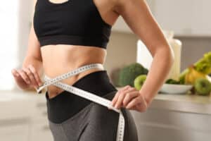 Woman measuring her waist with a tape measure for a liposuction and body contouring discussion